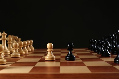 Photo of Chess pieces on wooden board against black background