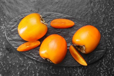 Photo of Delicious ripe persimmons on dark textured table, top view