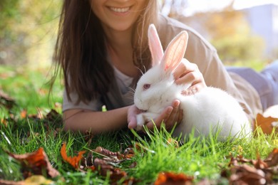 Happy woman with cute white rabbit on grass in park, closeup