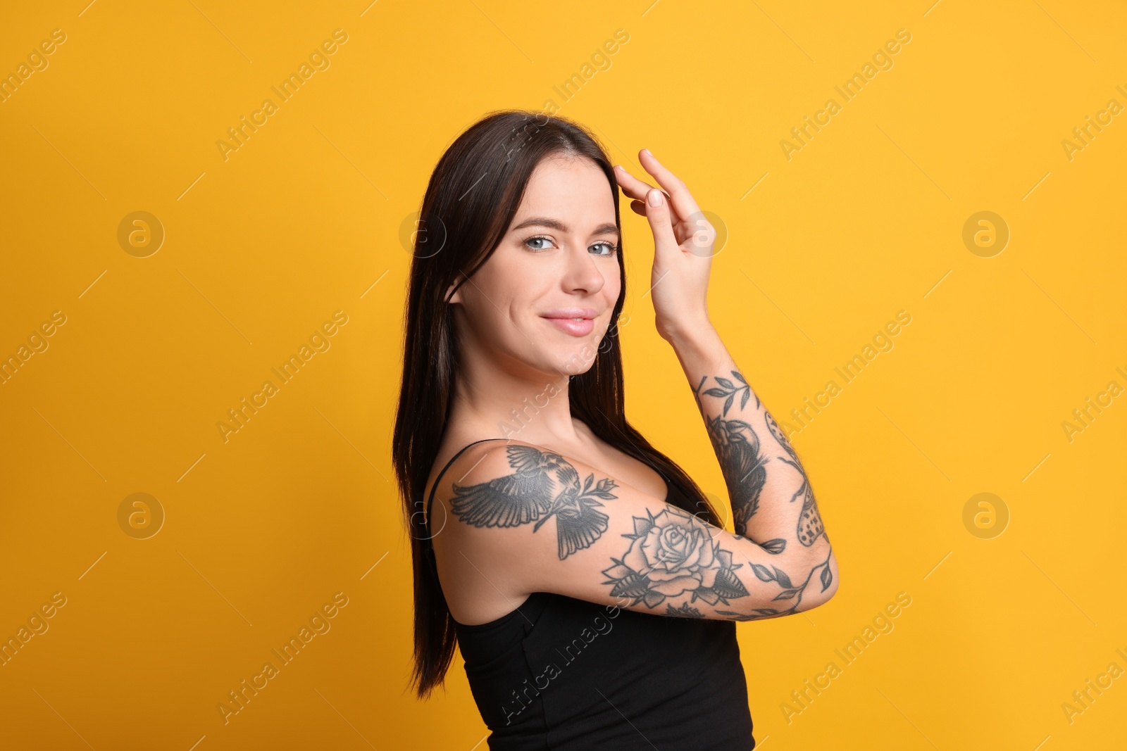 Photo of Beautiful woman with tattoos on arm against yellow background