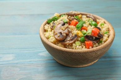 Delicious bulgur with vegetables and mushrooms on light blue wooden table, closeup. Space for text