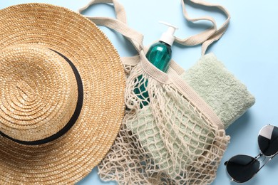 String bag, sunglasses, towel, straw hat and cosmetic product on light blue background, top view