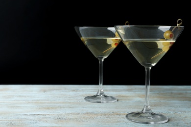 Photo of Glasses of Classic Dry Martini with olives on wooden table against black background. Space for text