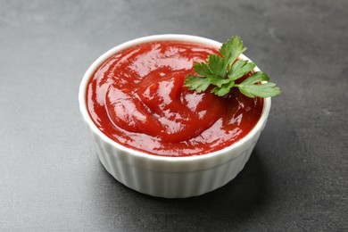 Photo of Delicious tomato ketchup and parsley in bowl on grey textured table, closeup