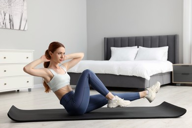 Photo of Young woman in sportswear doing exercises on fitness mat in bedroom