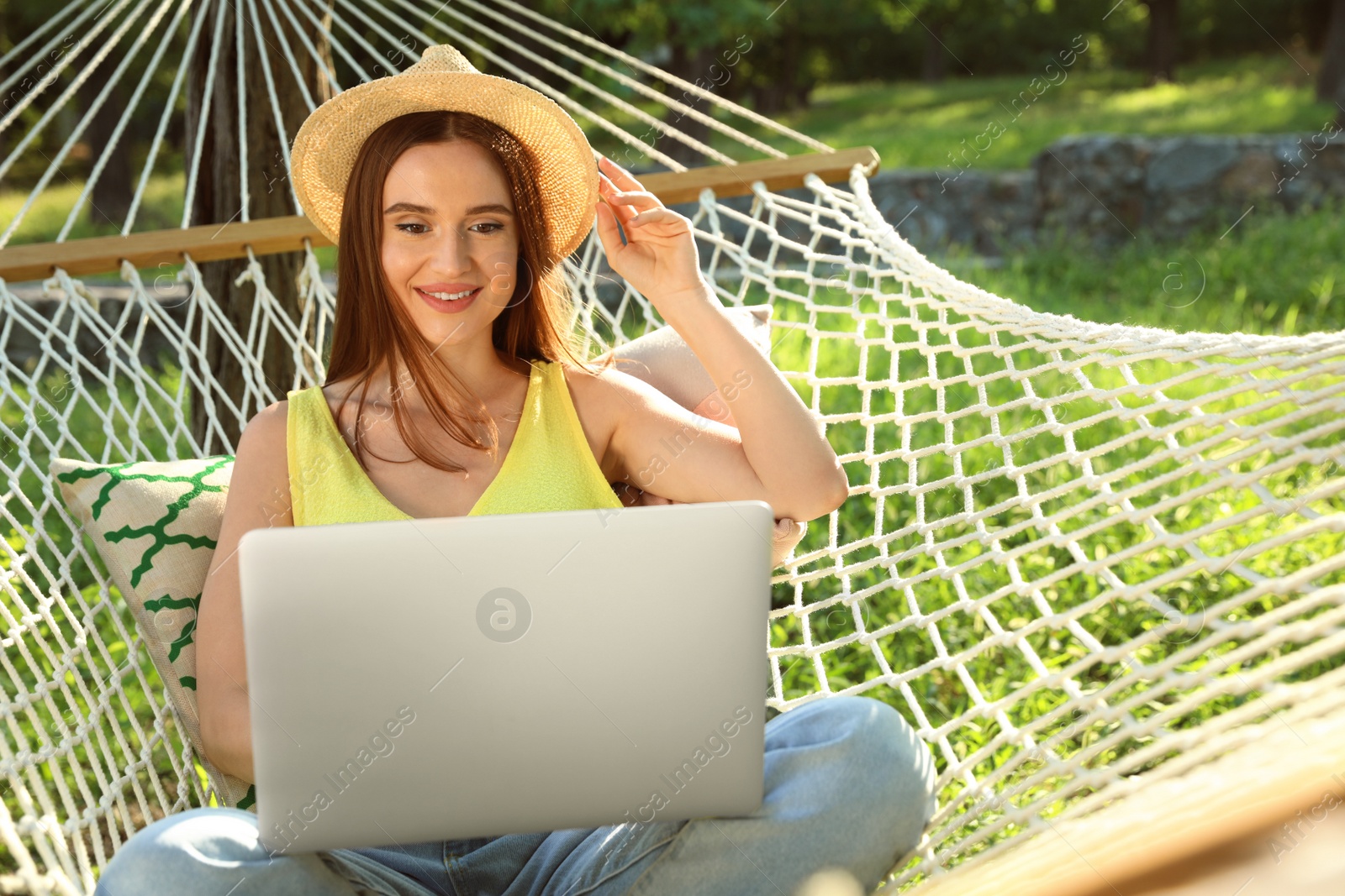 Photo of Young woman with laptop resting in comfortable hammock at green garden