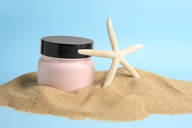 Jar with cream and starfish on sand against light blue background. Cosmetic product