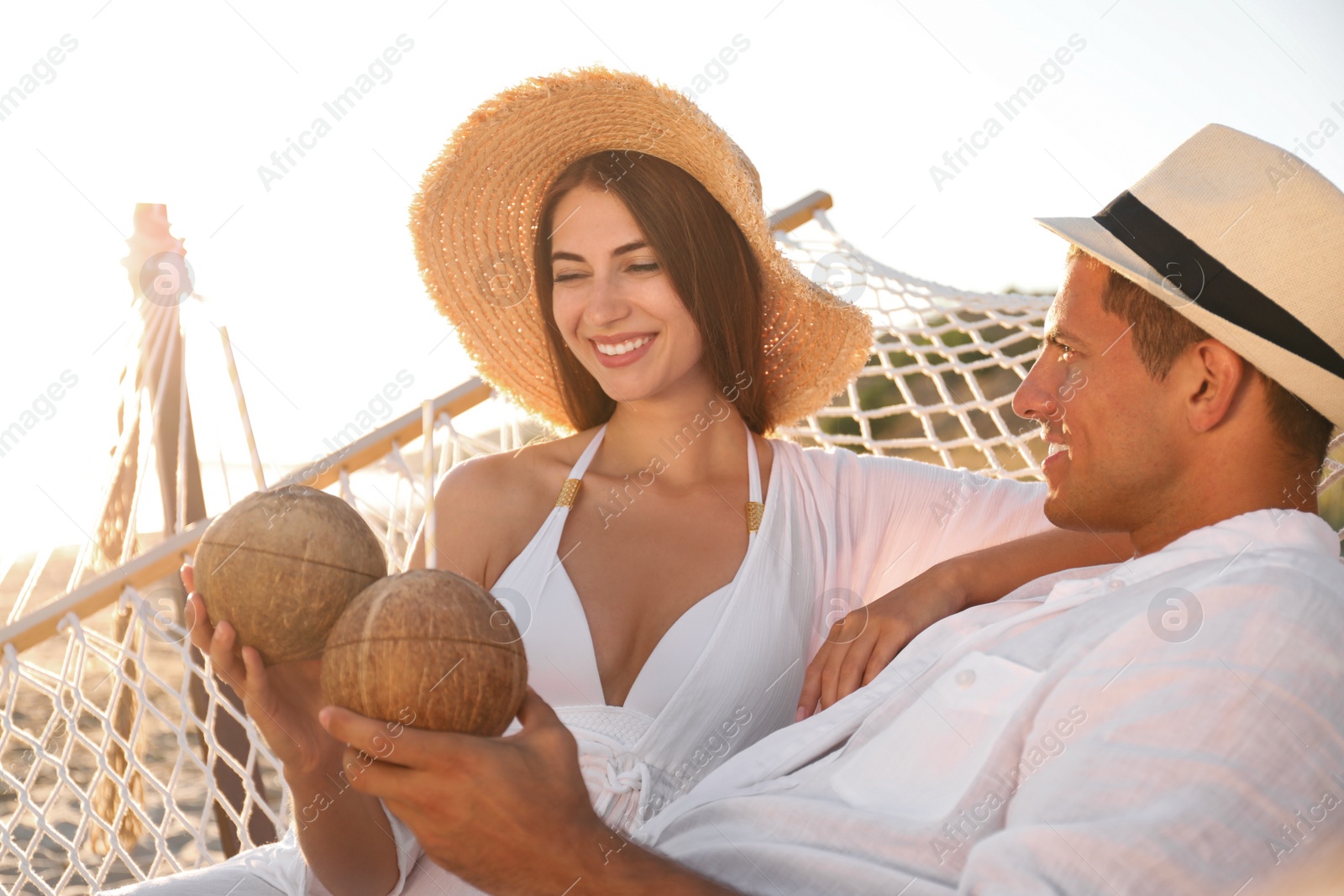 Photo of Happy couple with tropical cocktails relaxing in hammock on beach