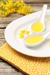 Photo of Rapeseed oil in gravy boats and beautiful yellow flowers on wooden table