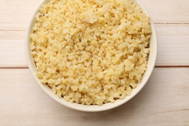 Photo of Delicious bulgur in bowl on wooden table, top view