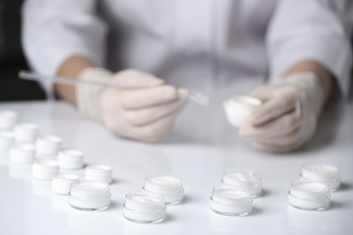 Photo of Scientist working in laboratory, focus on jars with different cosmetic products