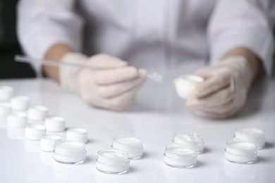 Scientist working in laboratory, focus on jars with different cosmetic products