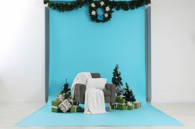 Photo of Beautiful Christmas themed photo zone with stylish armchair, trees and gift boxes in studio