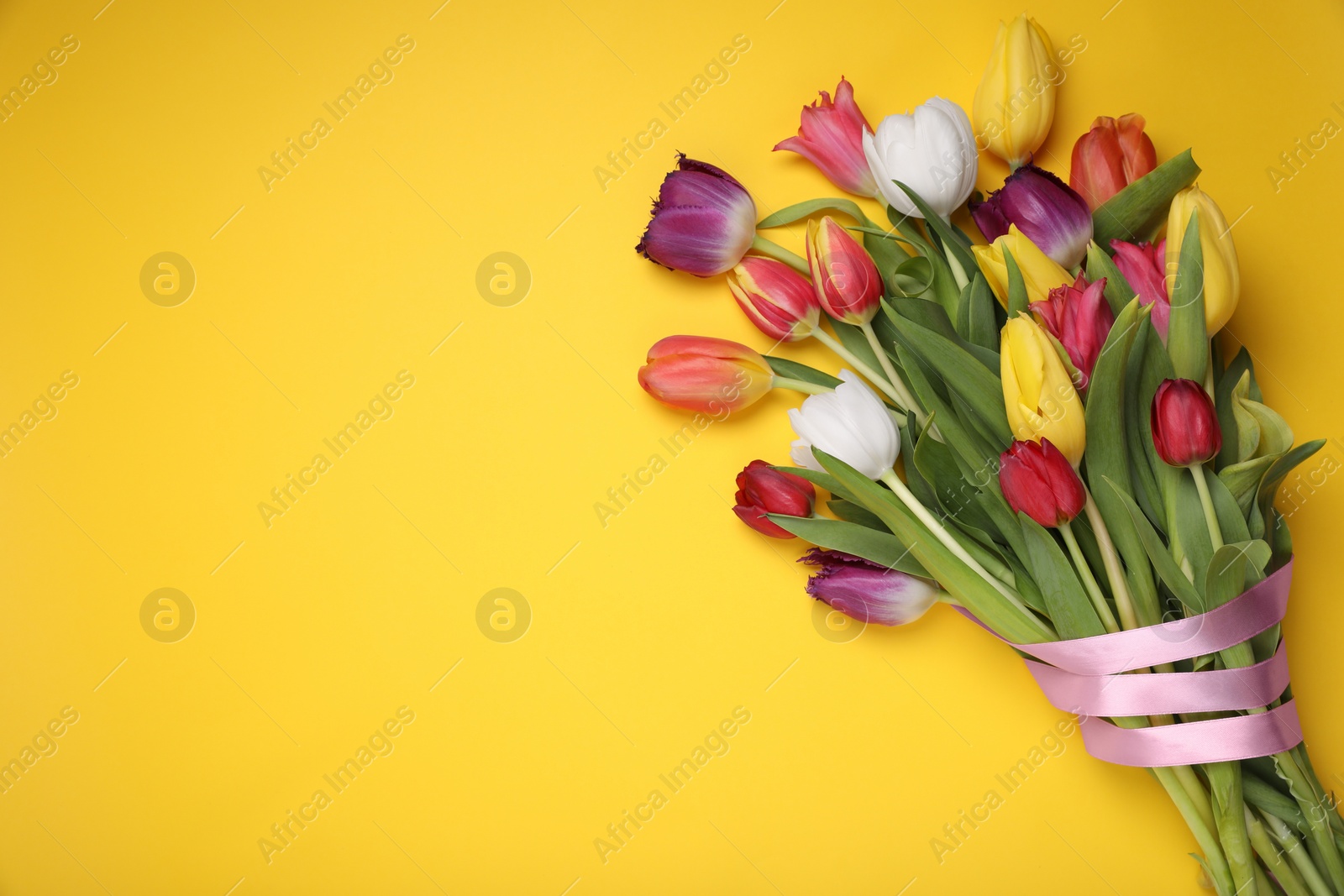 Photo of Bouquet of beautiful colorful tulip flowers tied with pink ribbon on yellow background, top view. Space for text