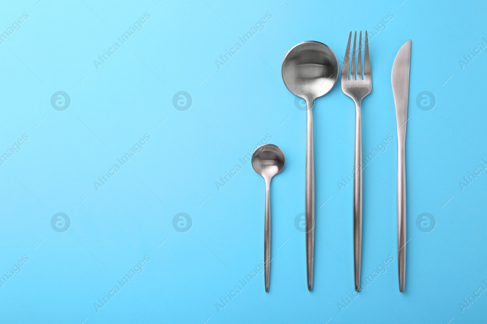 Photo of Stylish cutlery set on light blue table, flat lay. Space for text