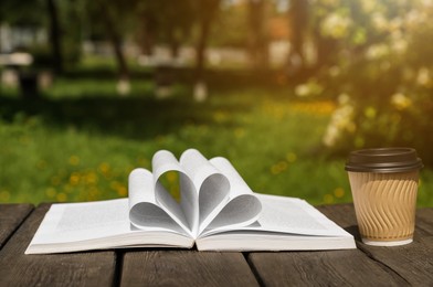 Photo of Open book and paper coffee cup on wooden table outdoors. Space for text