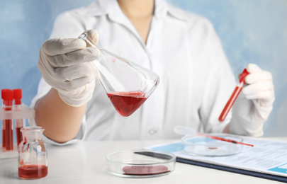 Photo of Scientist holding conical flask and tube with blood samples at table, closeup. Virus research