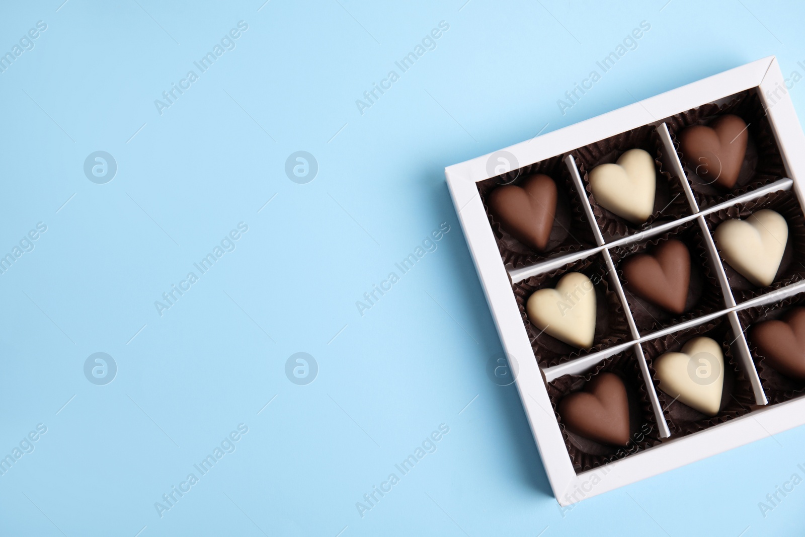 Photo of Tasty heart shaped chocolate candies on light blue background, top view with space for text. Happy Valentine's day