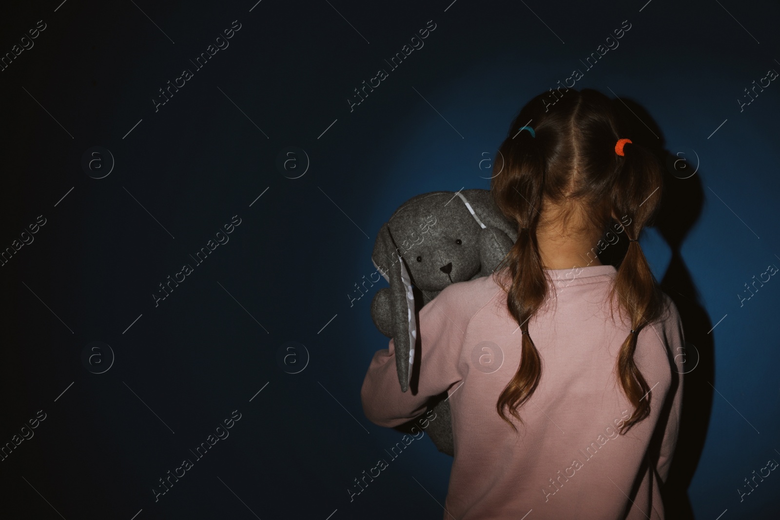 Photo of Little girl with toy near blue wall, back view and space for text. Domestic violence concept