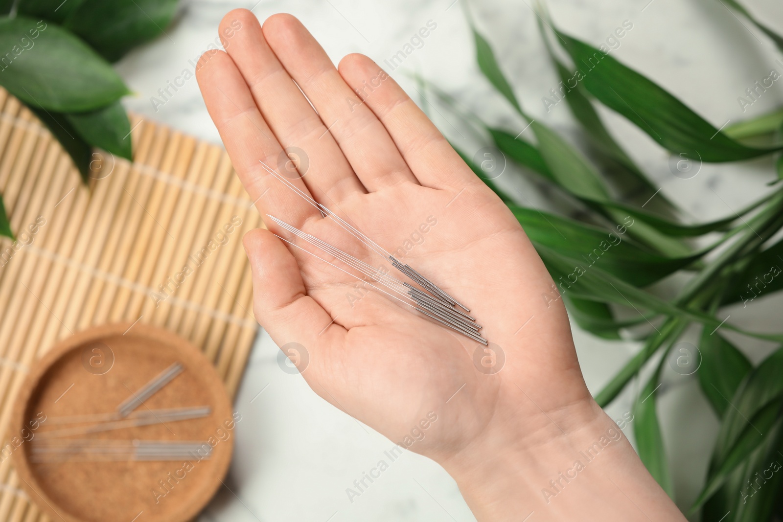 Photo of Woman holding many acupuncture needles over table, top view