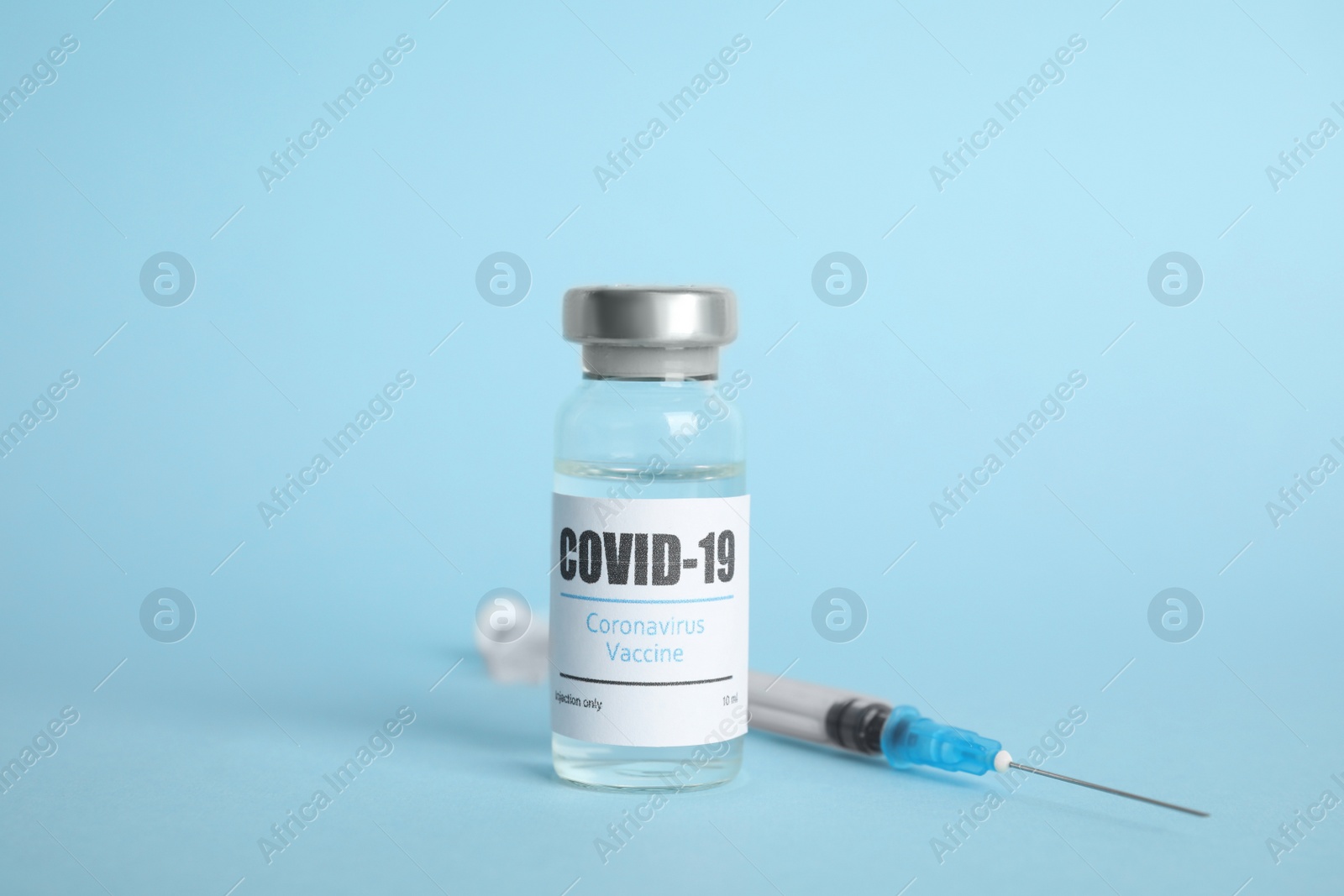 Photo of Vial with coronavirus vaccine and syringe on light blue background