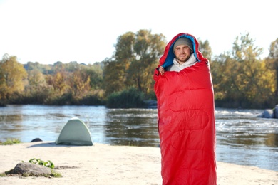 Male camper in sleeping bag on wild beach. Space for text