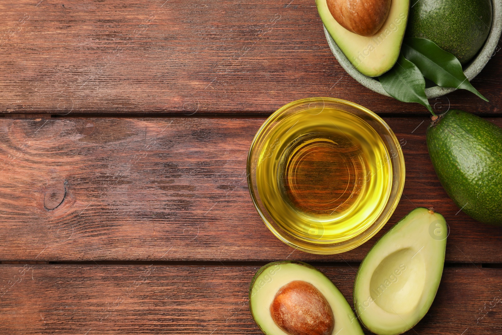 Photo of Cooking oil in bowl and fresh avocados on wooden table, flat lay. Space for text