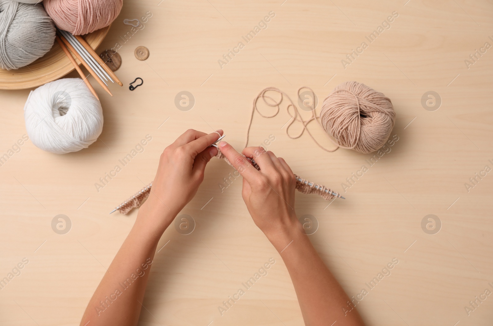 Photo of Woman knitting with threads at wooden table, top view. Engaging hobby