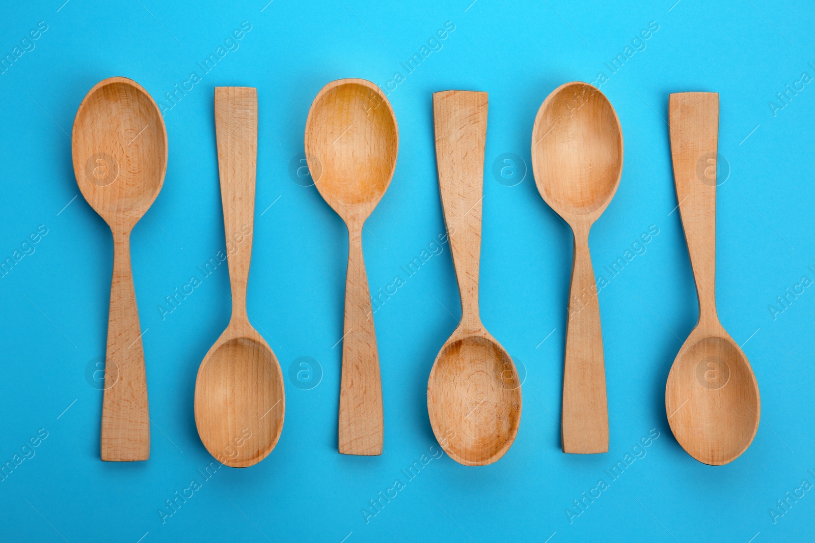 Photo of Clean empty wooden spoons on blue background, flat lay