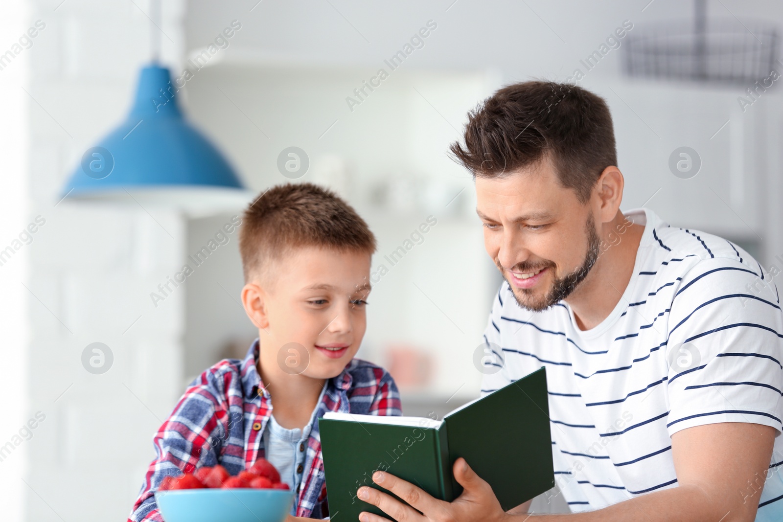 Photo of Dad and son reading interesting book in kitchen