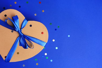 Photo of Beautiful heart shaped gift box with bow and confetti on blue background, top view. Space for text