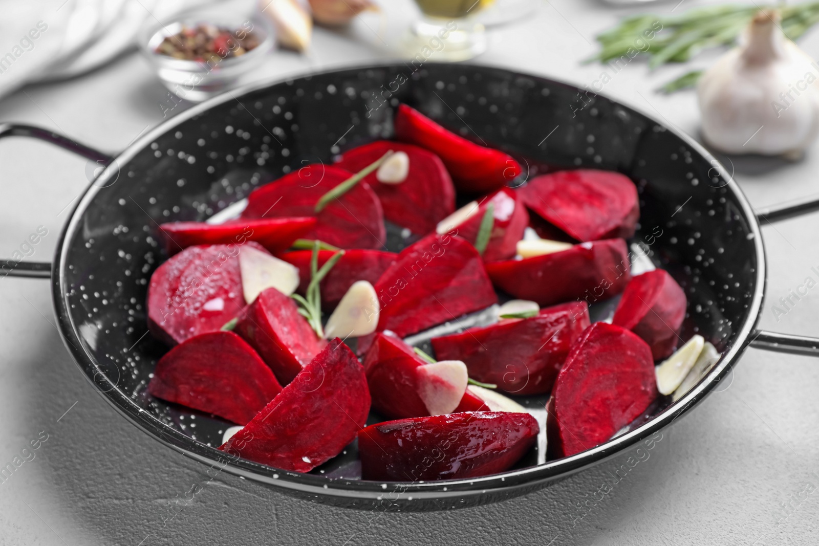 Photo of Slices of raw beetroot with garlic and rosemary in wok pan on white table, closeup