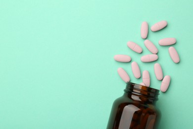 Vitamin pills and bottle on mint color background, top view. Space for text