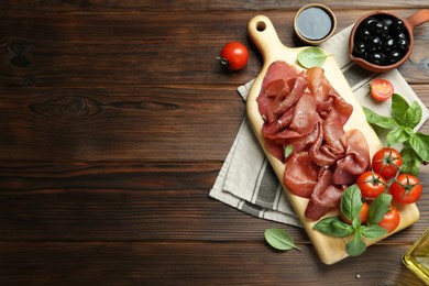 Photo of Board with delicious bresaola and other snacks served on wooden table, flat lay. Space for text