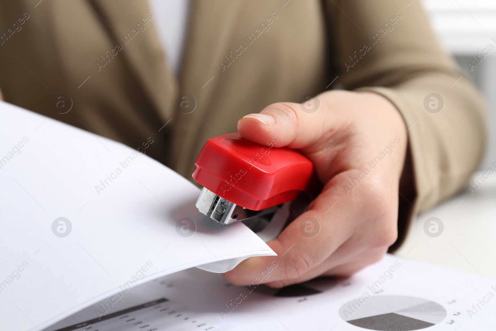 Photo of Woman with papers using stapler at white table, closeup