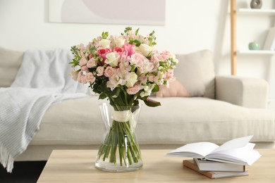 Photo of Beautiful bouquet of fresh flowers in vase and books on wooden table indoors