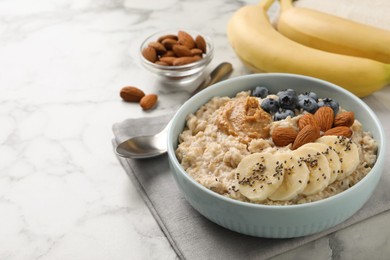 Tasty oatmeal porridge with toppings on white marble table, space for text