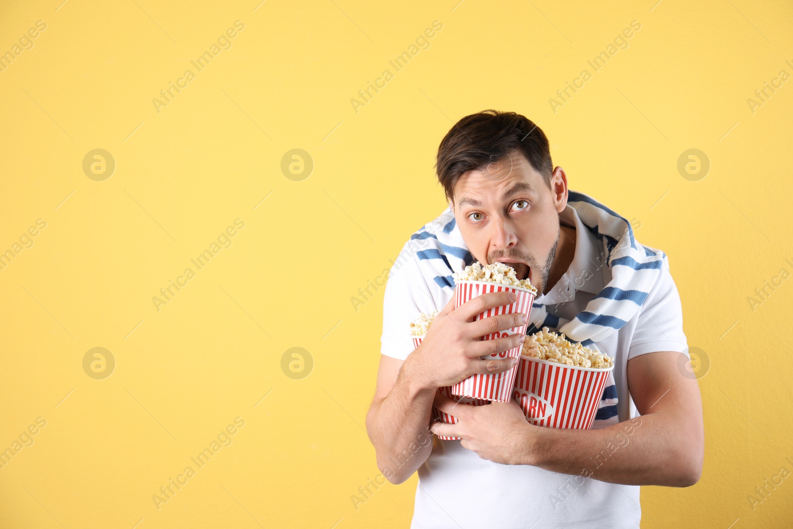Photo of Man eating tasty popcorn on color background. Space for text