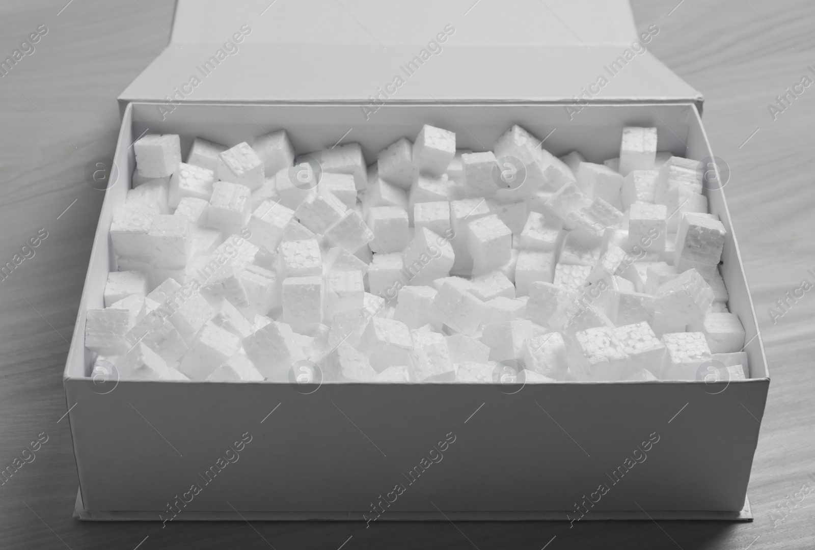 Photo of Cardboard box with styrofoam cubes on wooden floor, closeup