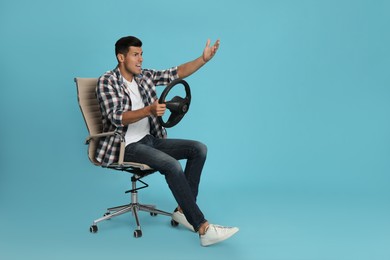 Photo of Emotional man on chair with steering wheel against light blue background. Space for text