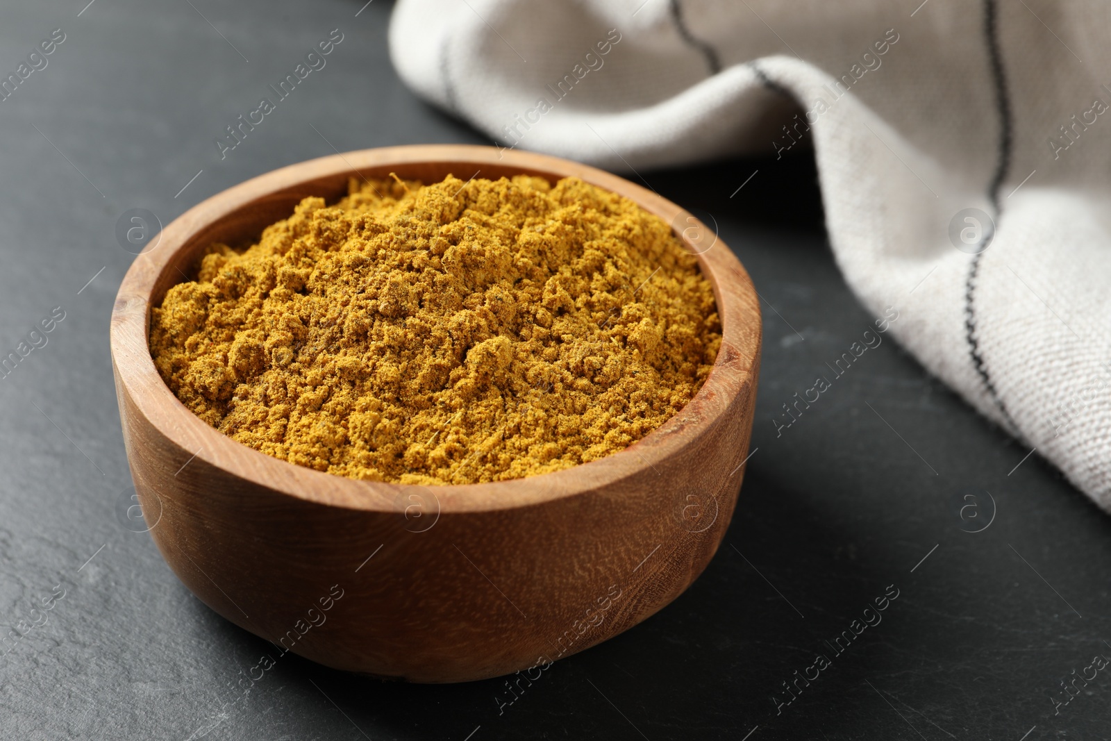 Photo of Dry curry powder in bowl on dark textured table, closeup