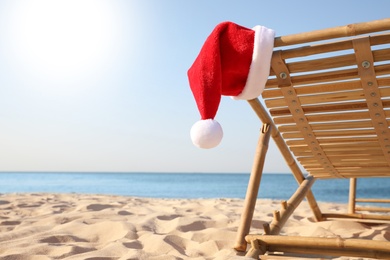 Photo of Sun lounger with Santa's hat on beach, closeup. Christmas vacation
