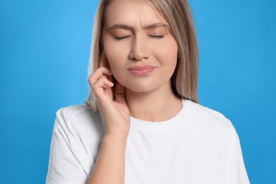 Photo of Young woman suffering from ear pain on light blue background