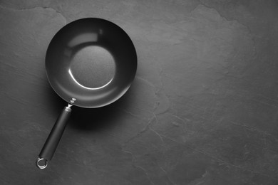 Empty iron wok on black textured table, top view. Space for text