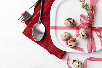 Photo of Festive Easter table setting with ribbon and quail eggs on white wooden background, flat lay