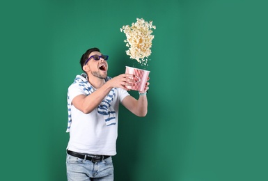Emotional man with 3D glasses throwing popcorn on color background. Space for text