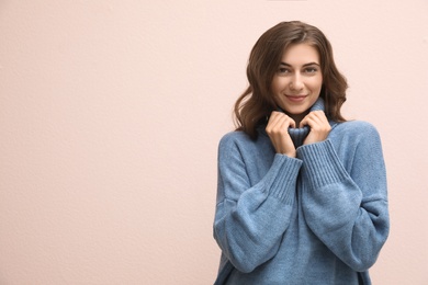 Photo of Beautiful young woman wearing warm blue sweater on light pink background. Space for text