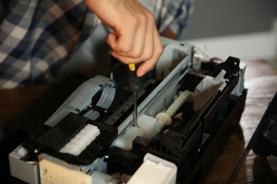 Photo of Repairman with screwdriver fixing modern printer, closeup