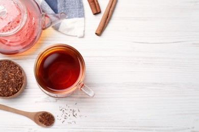 Photo of Freshly brewed rooibos tea, dry leaves and spoon on white wooden table, flat lay. Space for text