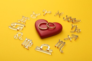 Photo of Zodiac signs, red heart and wedding rings on yellow background